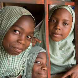 Nigerian girls looking through window smiling in classroom.