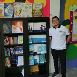 An Outreach Center coordinator poses next to a bookshelf full of children's books and games.