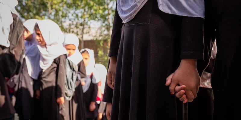 Two Afghan girls holding hands while waiting to enter school.