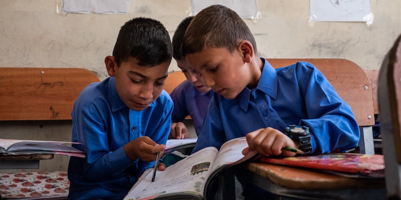 Three Afghan boys in class gathered around a book.