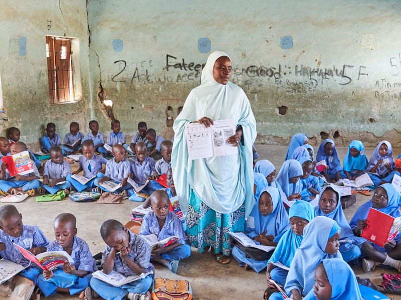 A teacher stands in a class full of students in Nigeria.