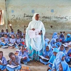 A teacher stands in a class full of students in Nigeria.