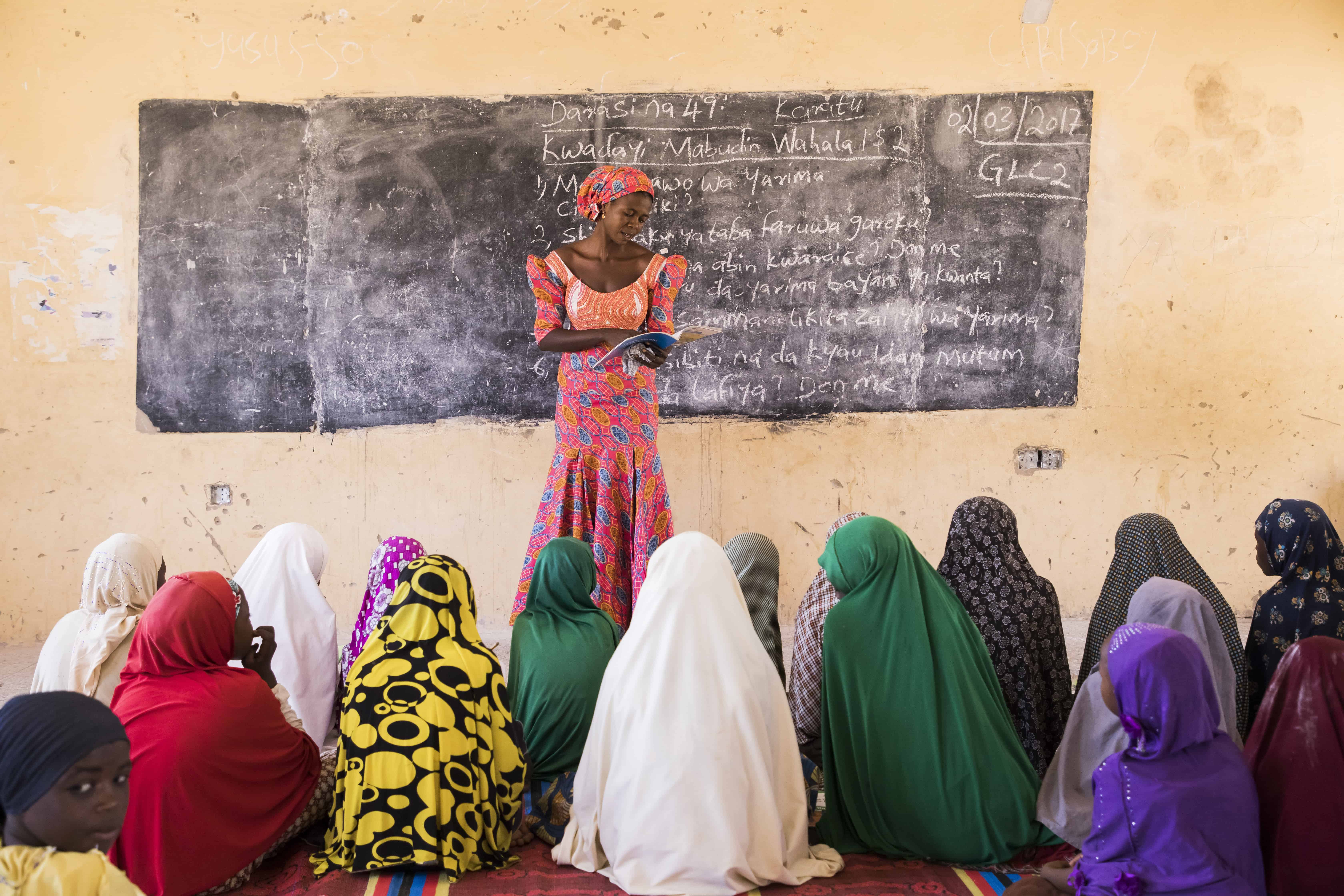 A female teacher in Nigeria stands in front of her class, reading from a book